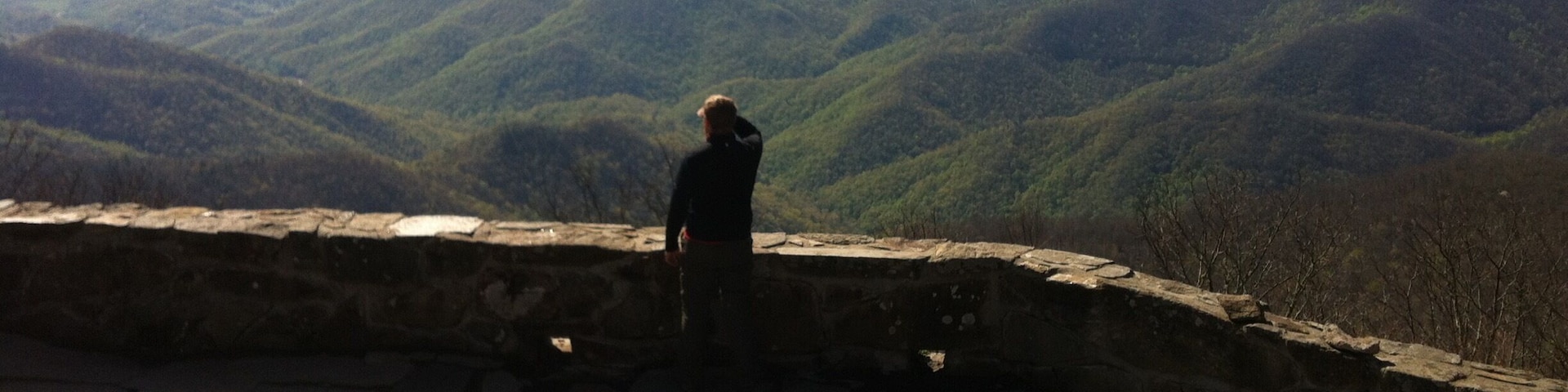 Eine Person steht auf einer steingepflasterten Plattform mit Blick auf eine gebirgige Landschaft.