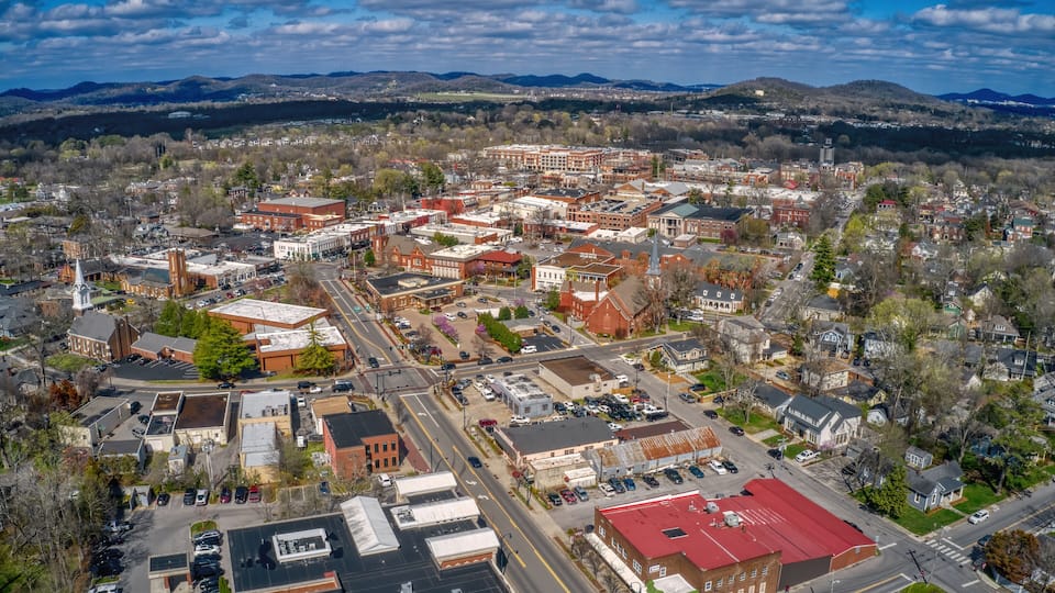 An aerial view of a town with historic buildings, a central square, and surrounding hills.