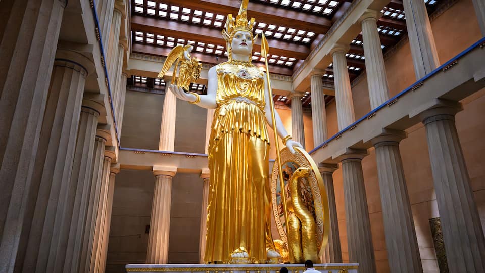 A golden statue in a grand hall with tall columns and a high ceiling.