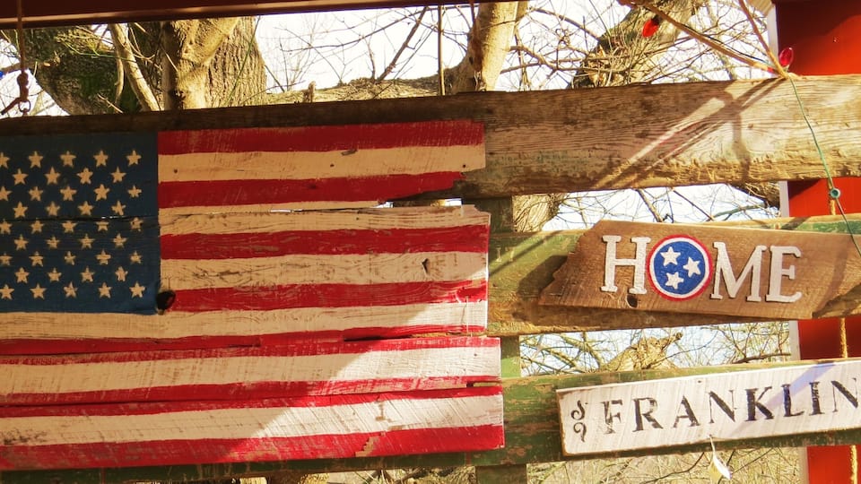 A wooden fence with an American flag and a 'HOME' sign, and a street sign reading 'FRANKLIN'.