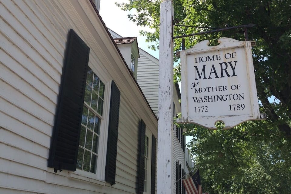 Una casa bianca con persiane nere e un cartello che recita: 'Casa di Mary, madre di Washington 1772-1789'.