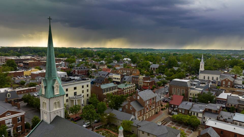 A town with historic buildings, a prominent church steeple, and a stormy sky.