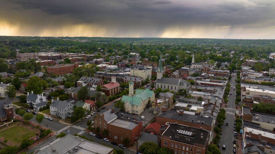 A cityscape with a prominent church steeple, a dense residential area, and a stormy sky.