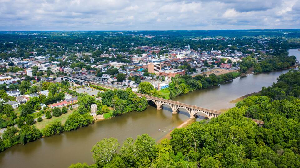 A river flowing through a town with a bridge, surrounded by greenery and buildings.