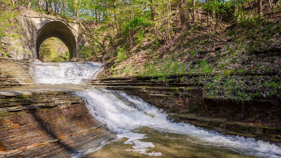 A stone bridge over a cascading waterfall in a forested area.