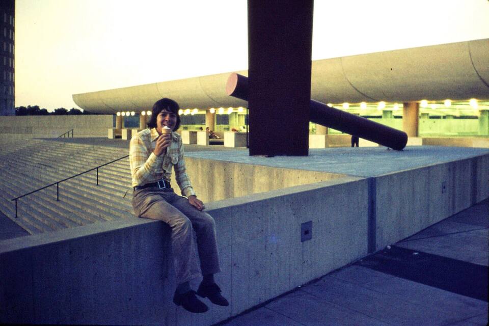 A person sitting on a concrete ledge with a large cylindrical structure behind them.