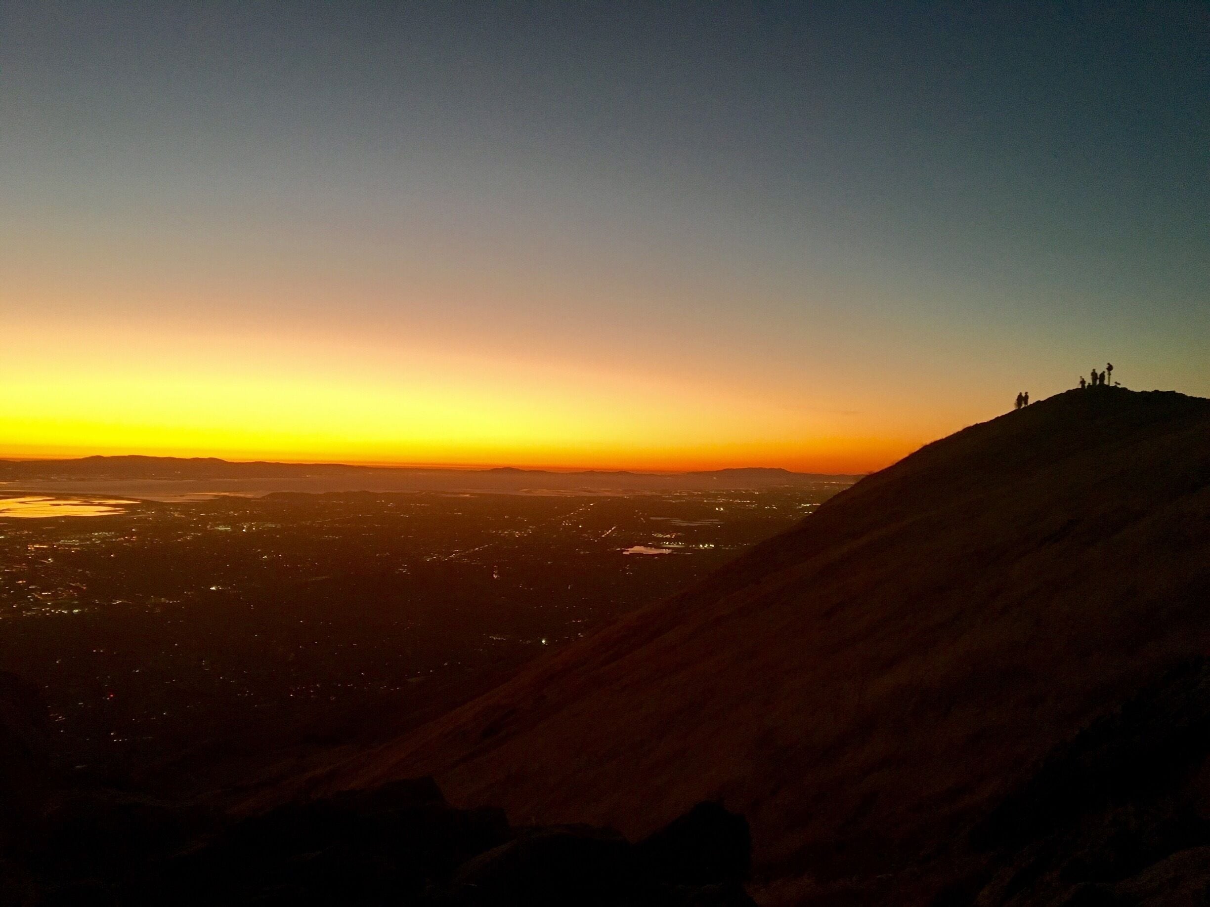 A sunset over a cityscape with a hill in the foreground.