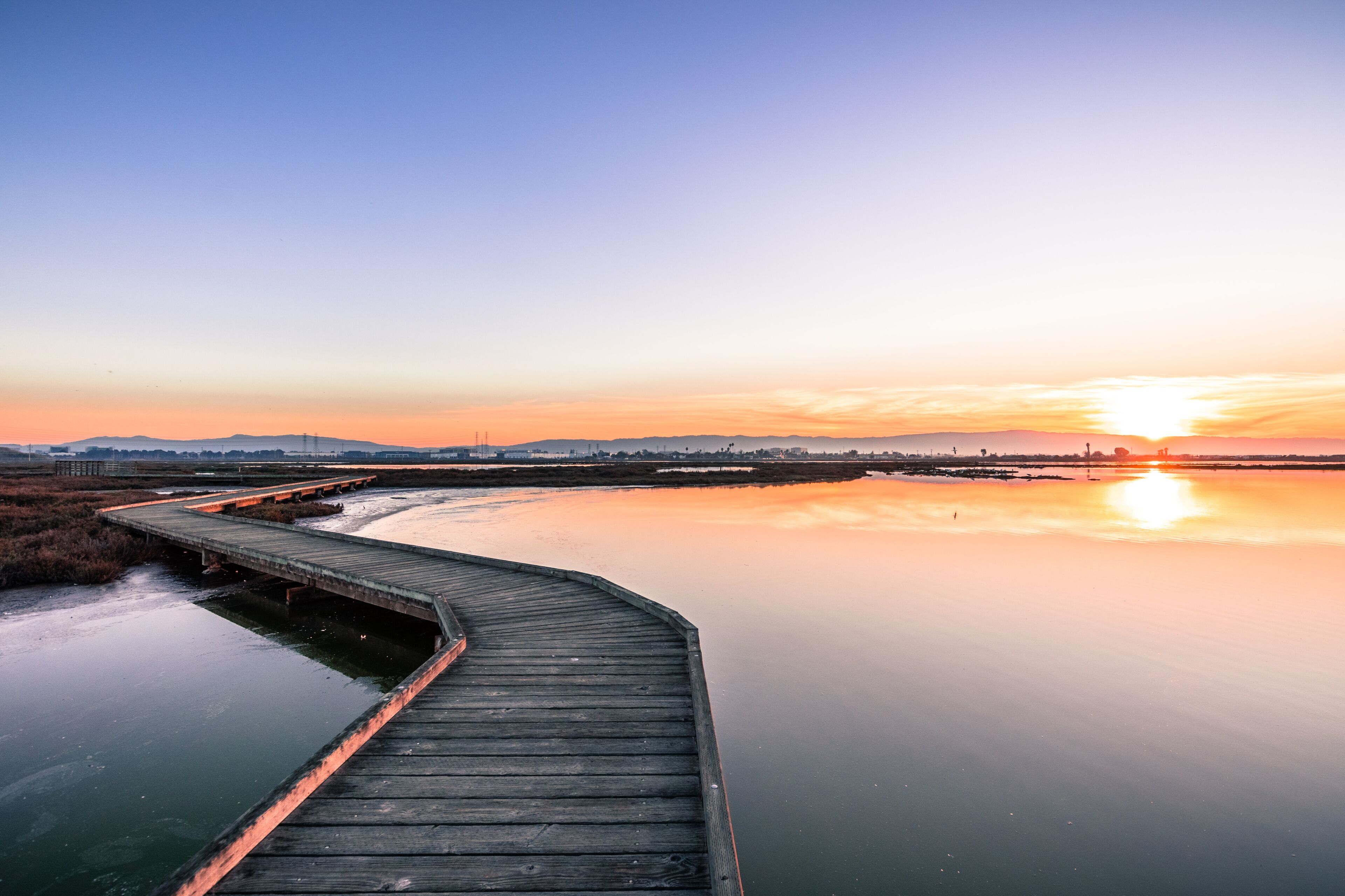 A wooden boardwalk leading to a calm body of water at sunset.