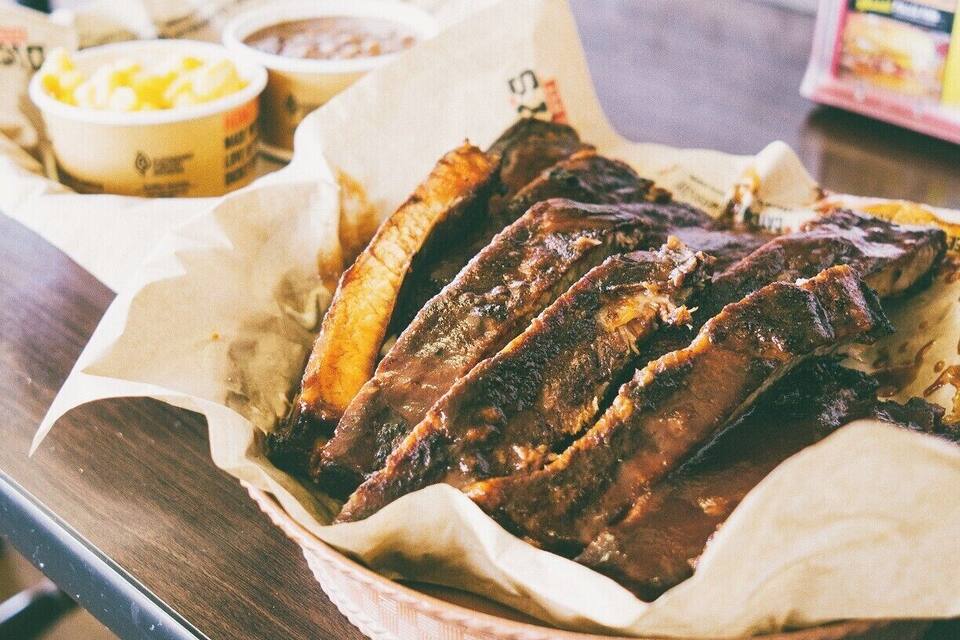 A basket of barbecued ribs on a wooden table.