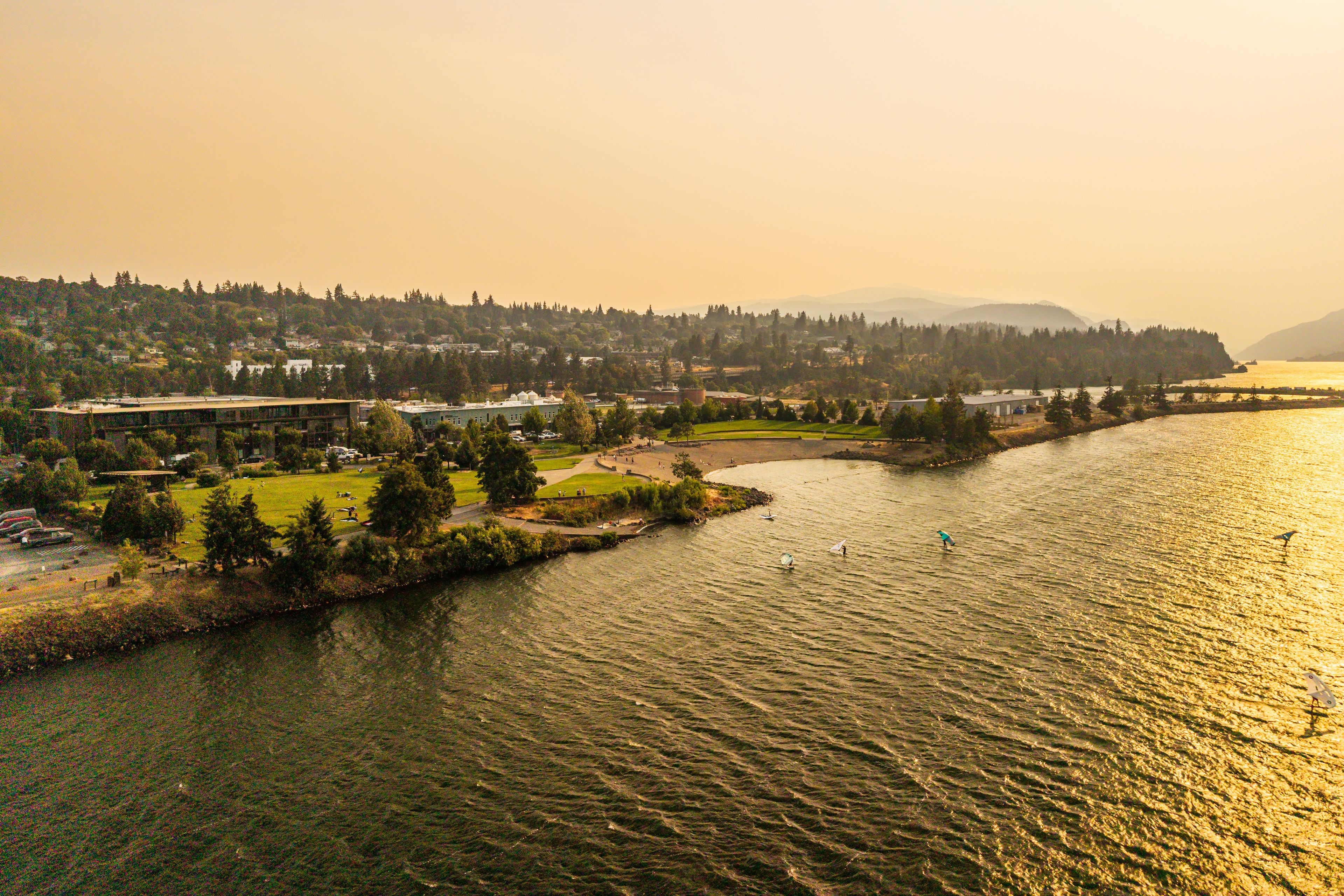 A river with boats, a park, and buildings along the riverbank.