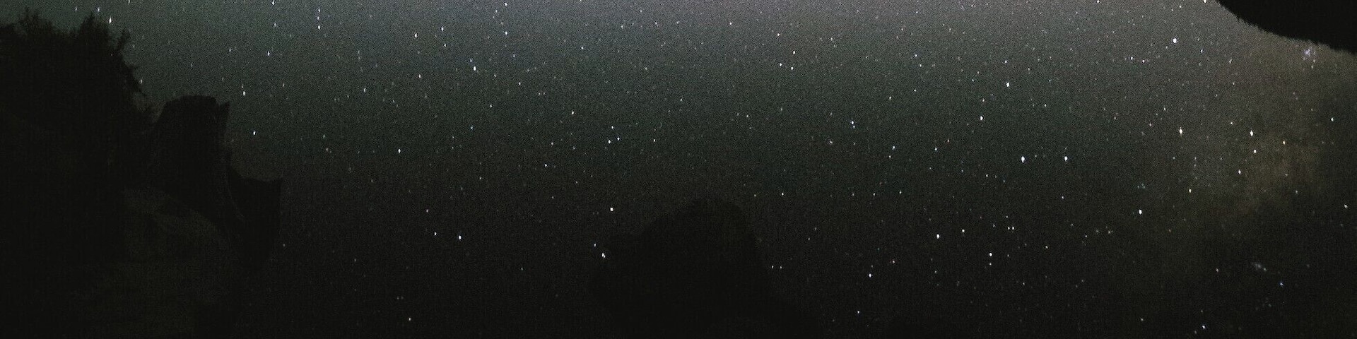 A starry night sky over a mountain range reflected in a calm lake.