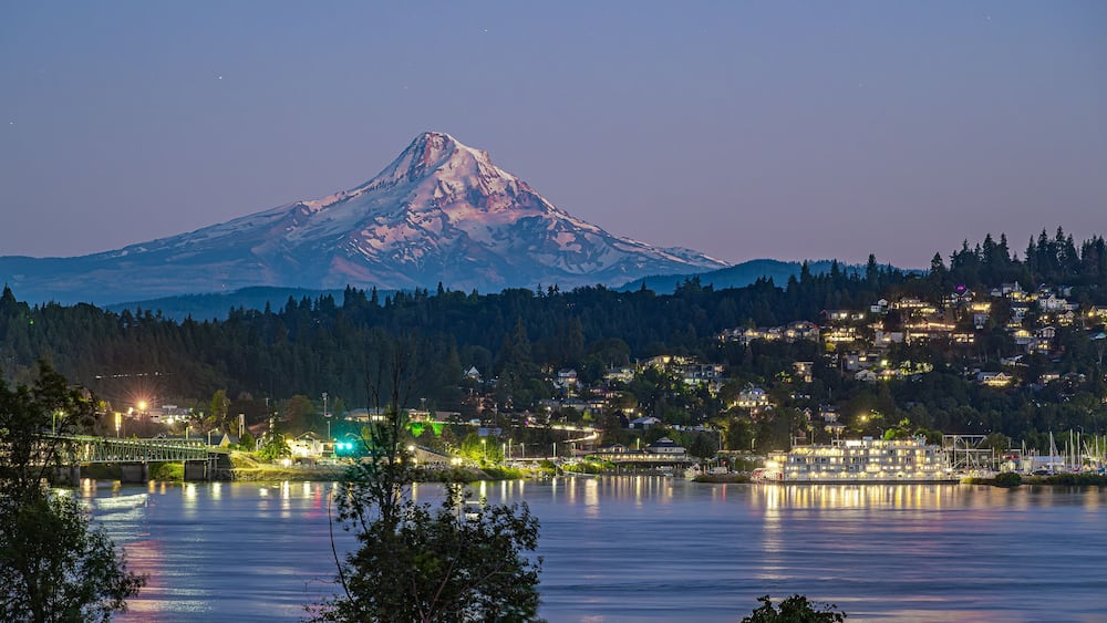Une montagne dont le sommet est coiffé de neige, une étendue d’eau reflétant les lumières et une ville dont les bâtiments sont illuminés.