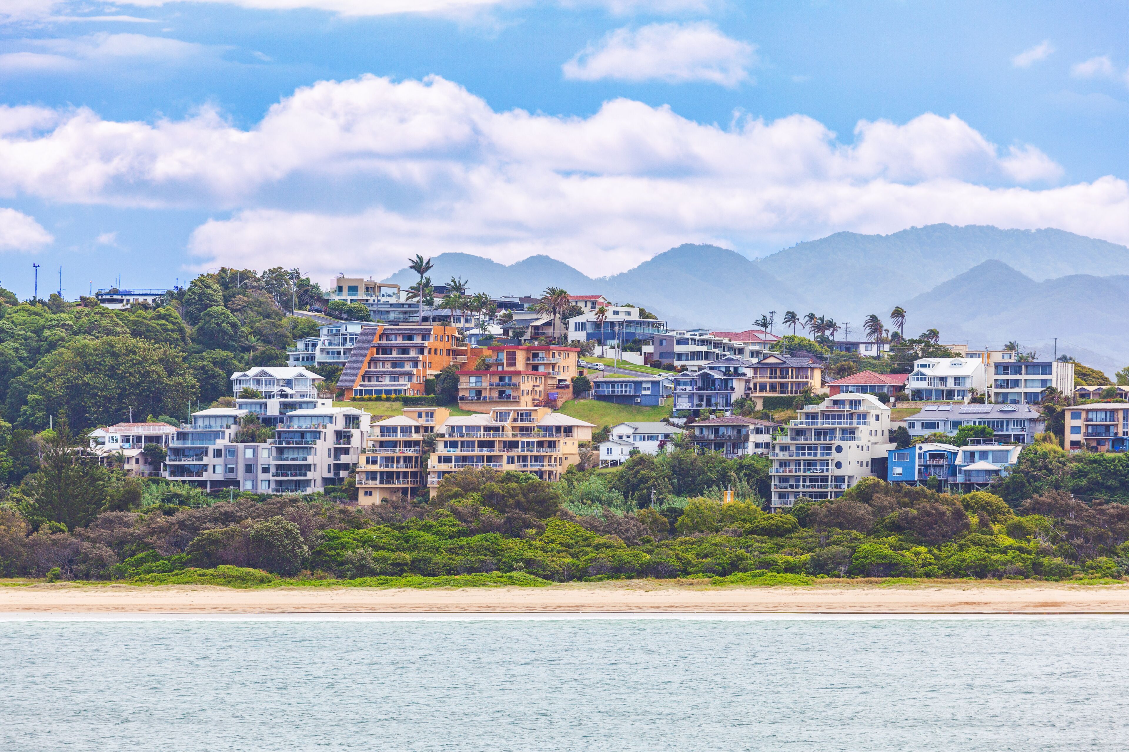 Uma área residencial costeira com edifícios altos, uma praia e montanhas ao fundo.