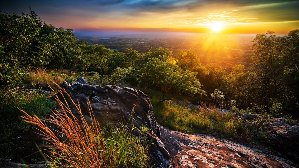 A sunset over a mountainous landscape with dense greenery and rocky terrain.