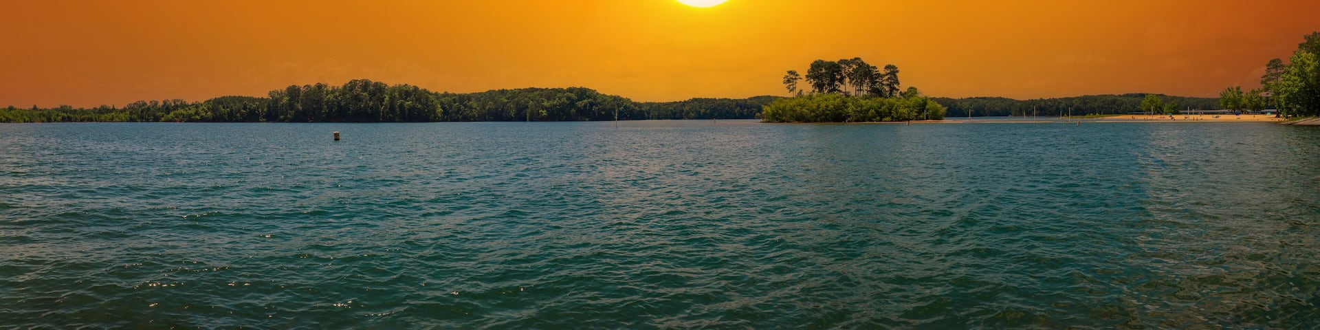 A sunset over a lake with a small island and a distant shoreline.
