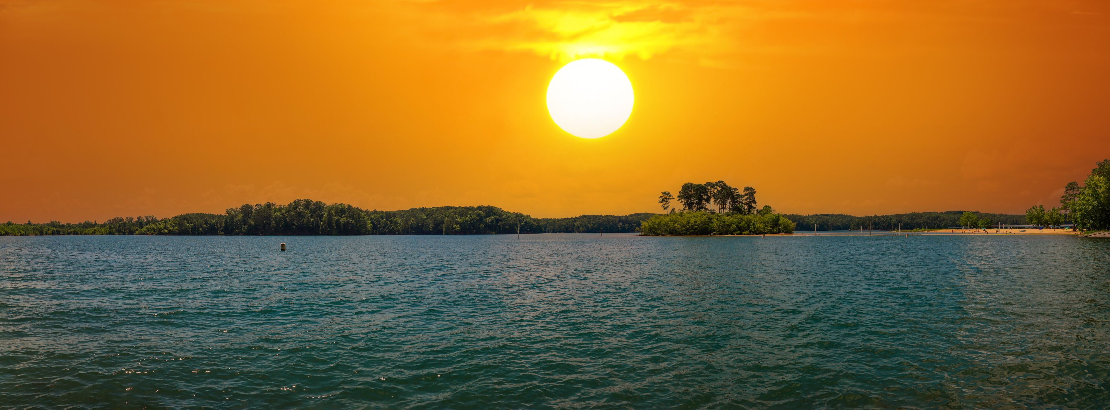 a stunning panoramic shot of the rippling blue waters of Lake Allatoona with powerful clouds at sunset surrounded by lush green trees, grass and plants at Victoria Beach in Acworth Georgia USA