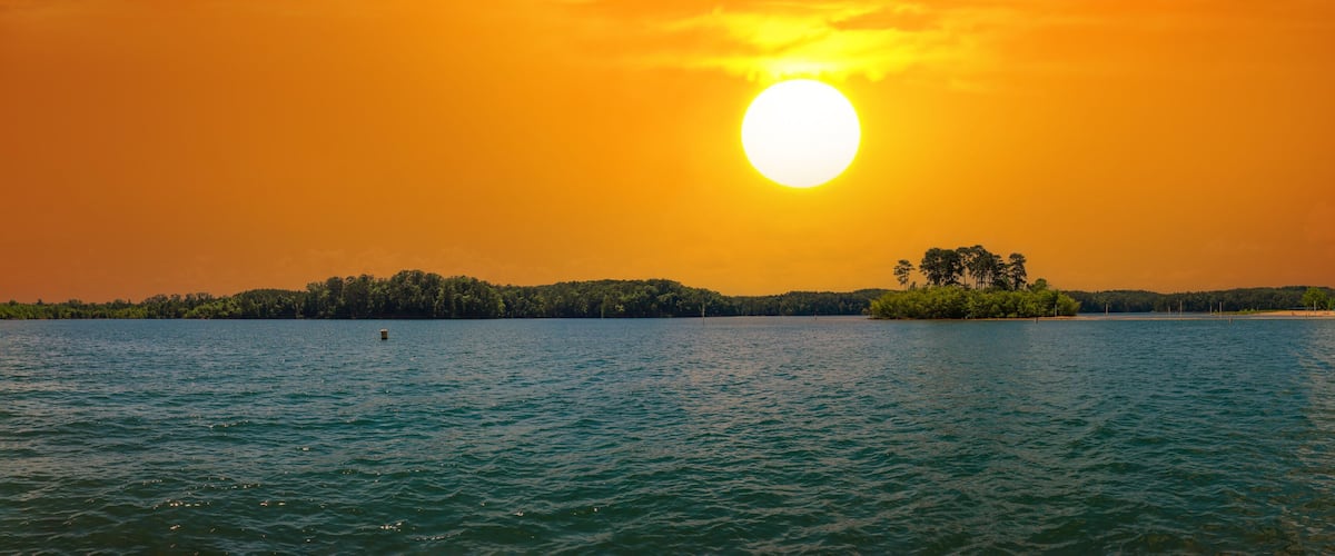 a stunning panoramic shot of the rippling blue waters of Lake Allatoona with powerful clouds at sunset surrounded by lush green trees, grass and plants at Victoria Beach in Acworth Georgia USA