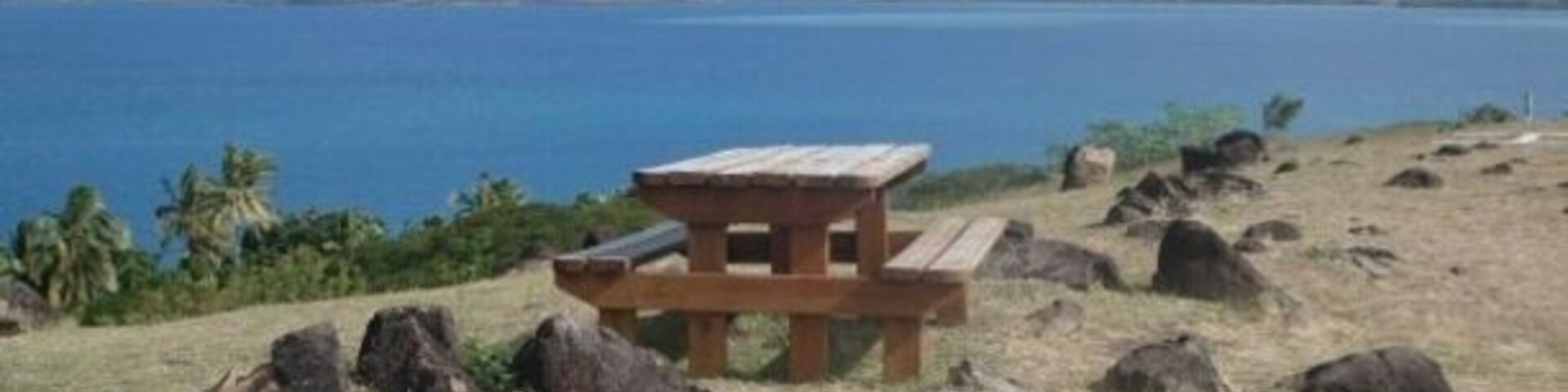 Una mesa de picnic en una colina cubierta de hierba con vistas a un cuerpo de agua y montañas al fondo.