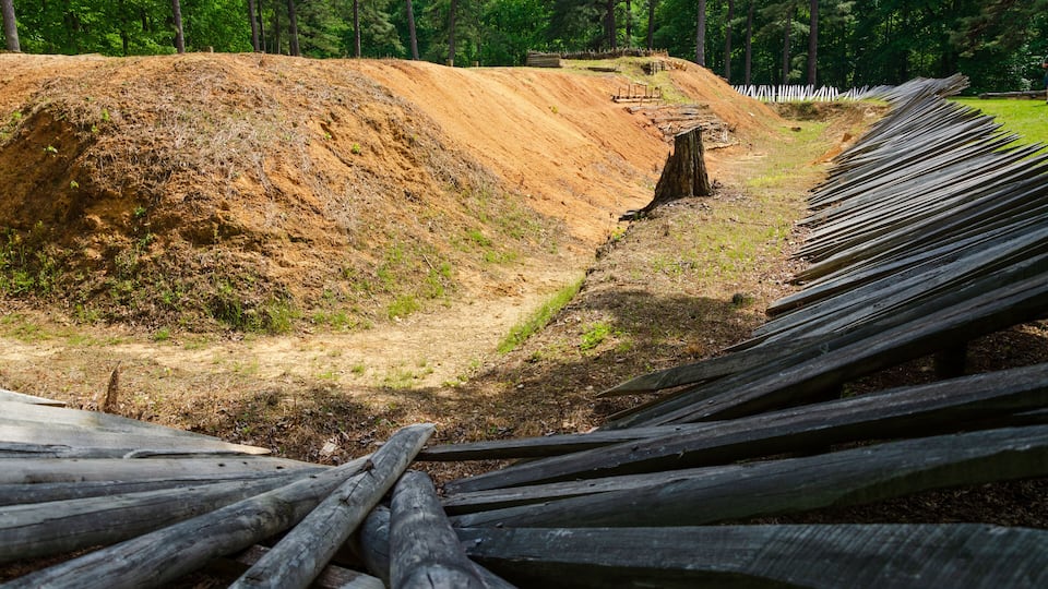 A dirt embankment with a wooden fence and a tree stump.