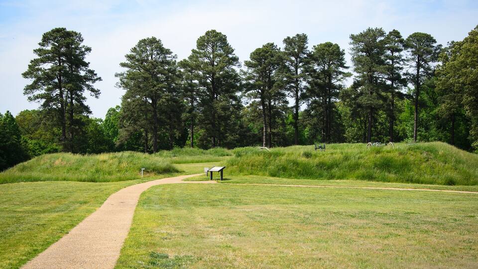 A grassy field with a gravel path leading to a bench and a signpost.