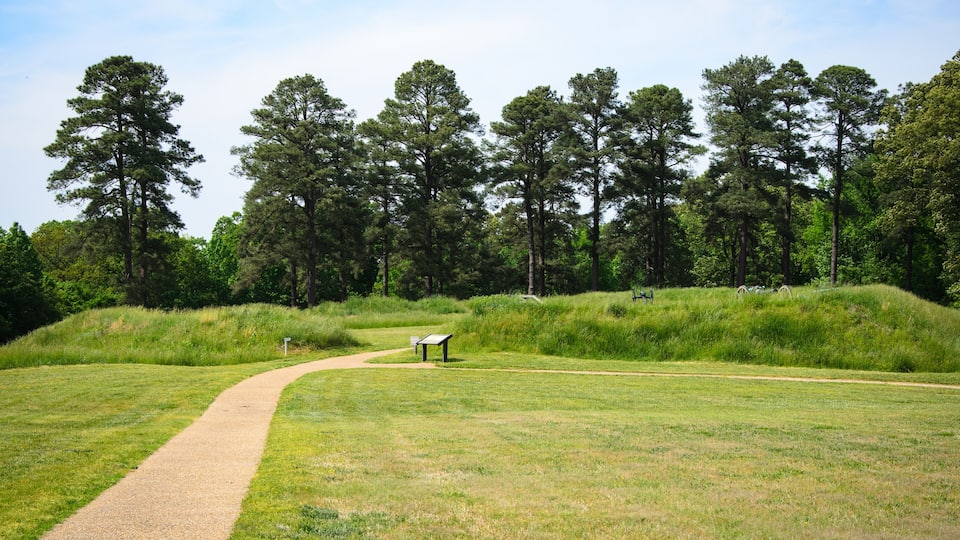 A park with a gravel path, grassy areas, and a wooden bench.