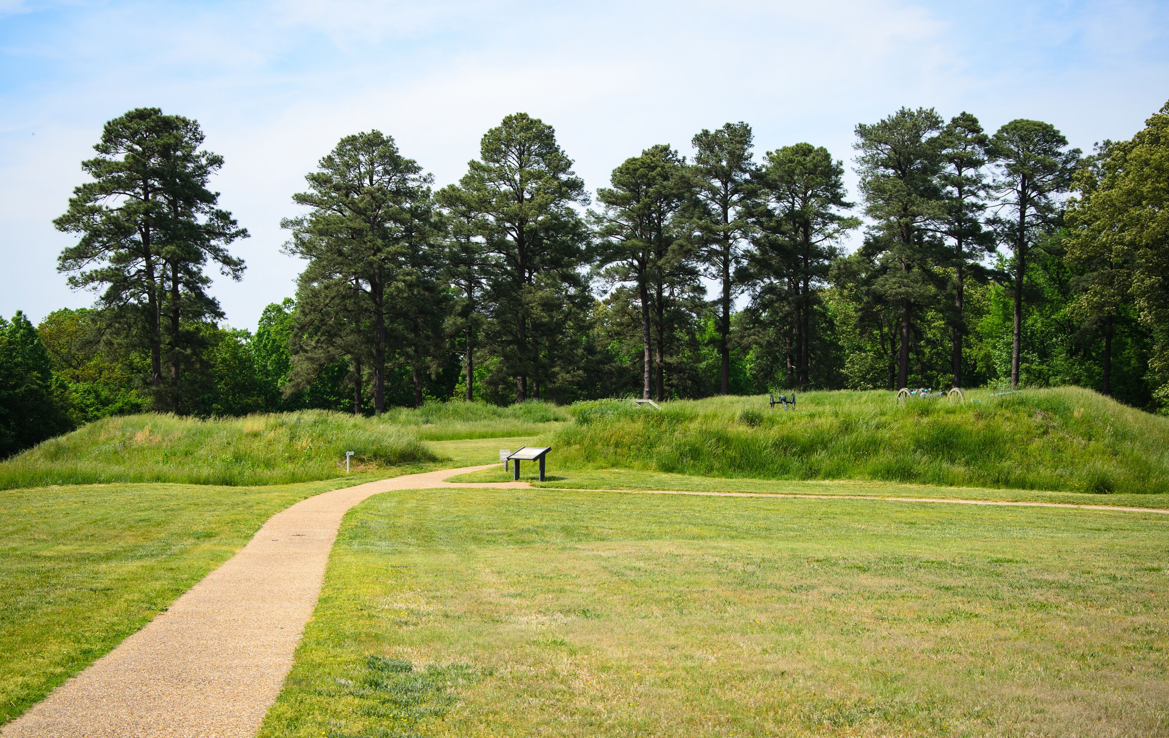 A park with a gravel path, grassy areas, and a wooden bench.