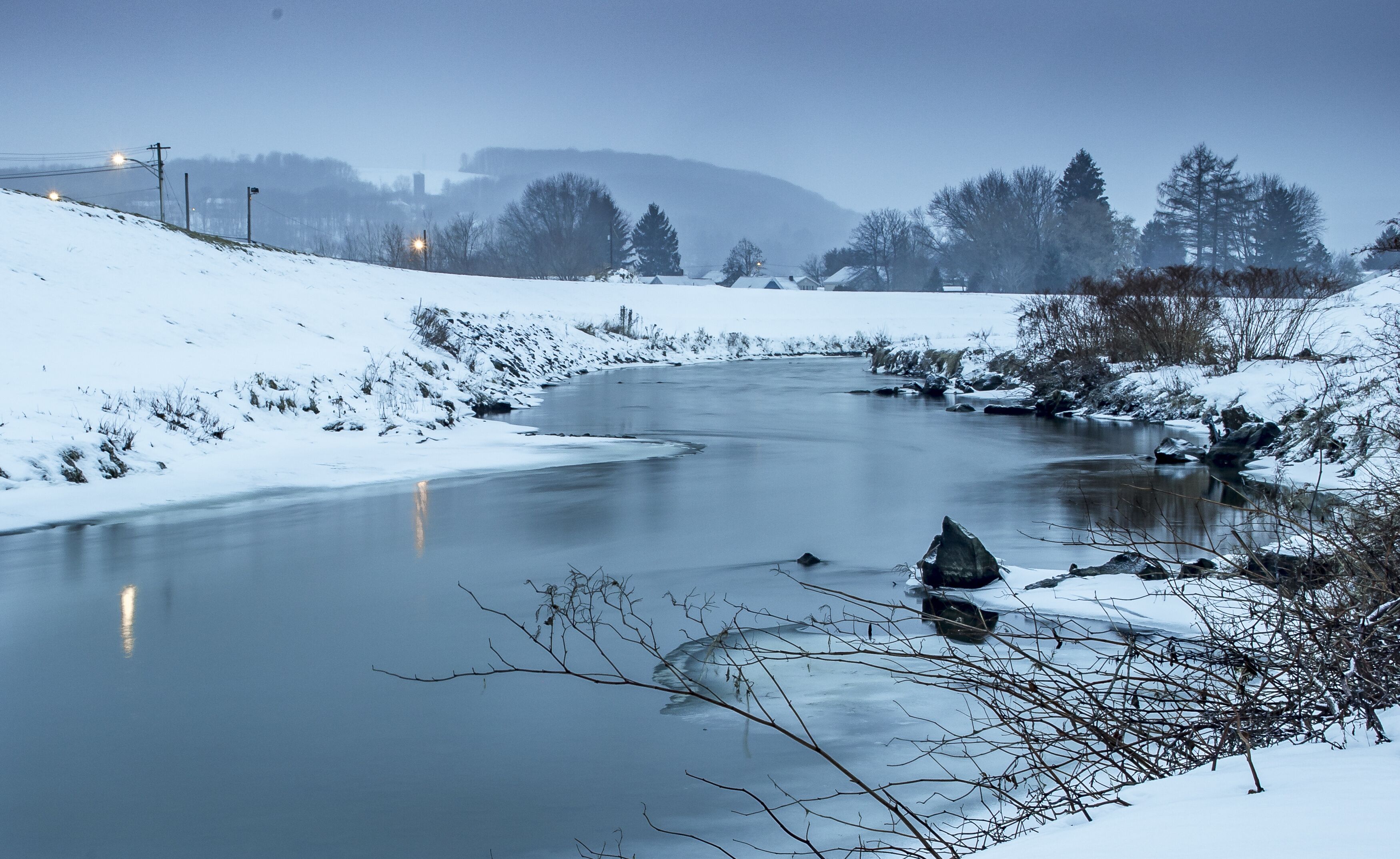 Une rivière enneigée, sinueuse, bordée d’arbres et dominée par une chaîne de montagnes lointaine.