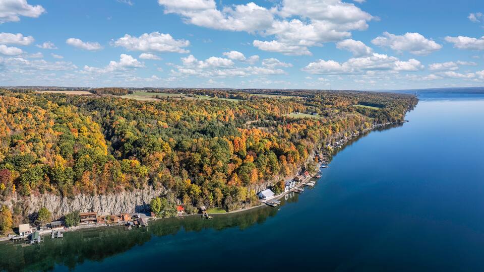 A lake surrounded by autumn-colored trees, a dock, and a distant lighthouse.