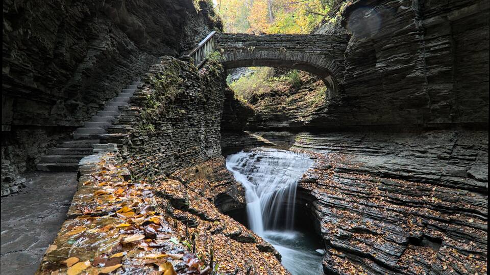 rainbow falls at watkins glen state park (waterfall in a gorge with stone bridge, staircase, glacial layered rock formation) falling water, stream, autumn colors, leaves changing, fall foliage