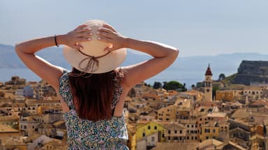 A woman holding a straw hat overlooking a historic town with a prominent fortress on a hill.