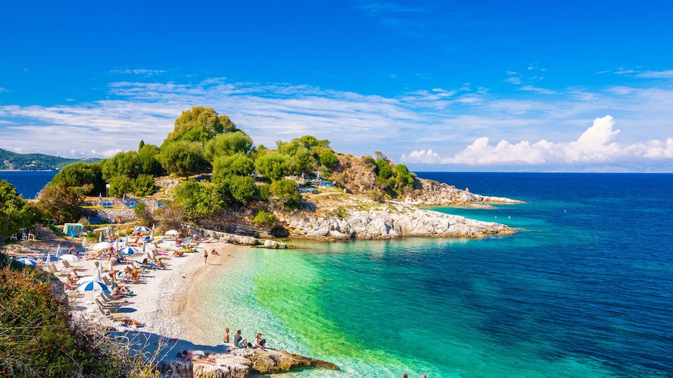 A coastal beach with clear turquoise waters, rocky outcrops, and lush greenery.