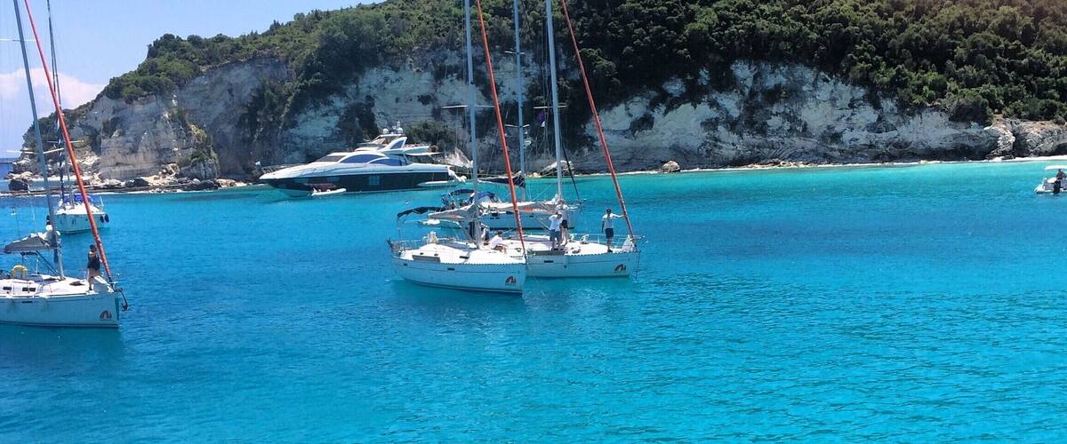 A clear turquoise sea with several sailboats anchored near a rocky coastline.