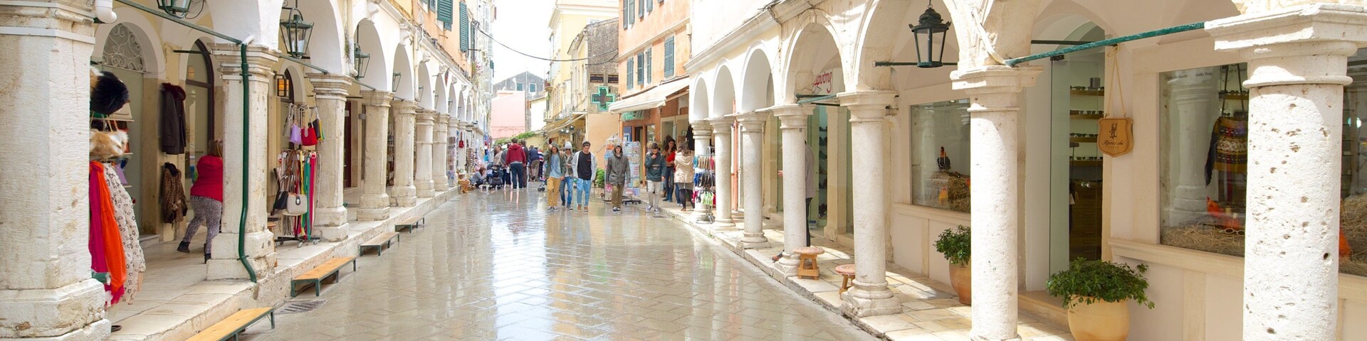 Uma rua de paralelepípedos molhada, ladeada por edifícios brancos, arcos e lojas.