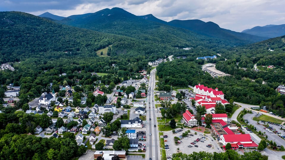A town with a main road, surrounded by green hills and mountains.