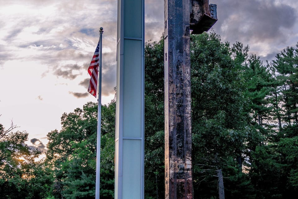 A tall, rectangular monument with a flagpole, surrounded by a grassy area and trees.