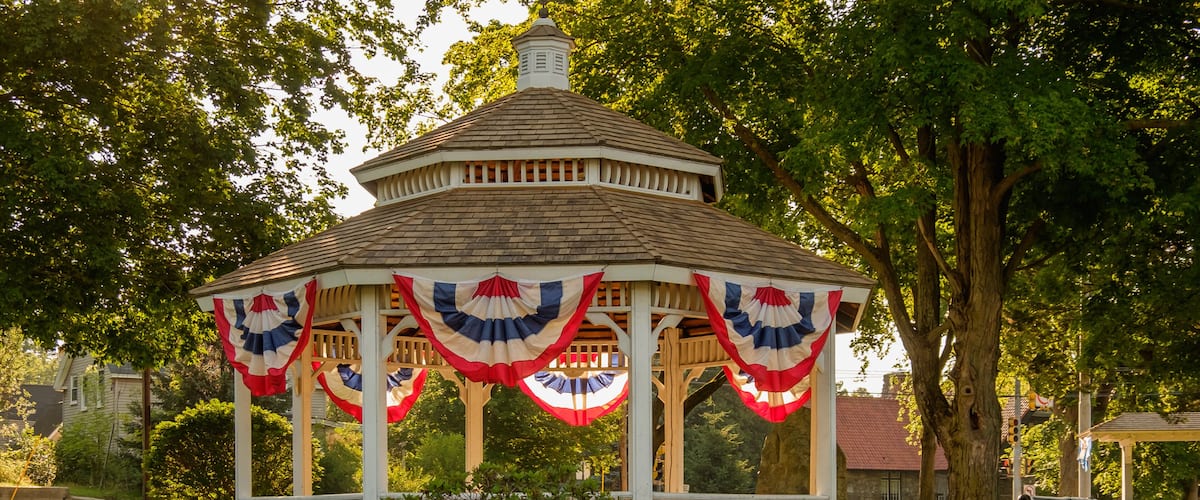 A gazebo with red, white, and blue drapes, surrounded by lush greenery and trees.