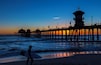 A pier extending into the ocean at sunset with a lighthouse at the end.