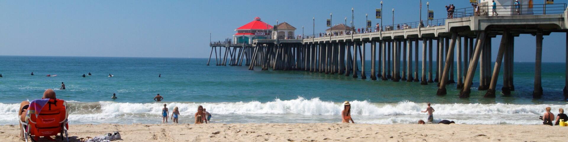 A beach with a pier extending into the ocean, featuring a red-roofed building and a lookout tower.