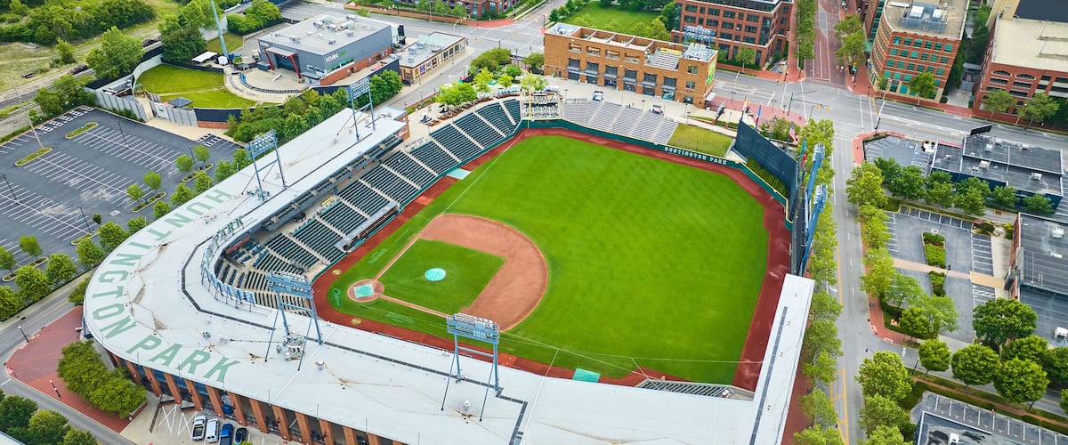 A baseball stadium with a large field, seating areas, and a parking lot.