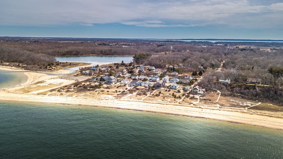An aerial view of a coastal residential area with houses, a beach, and a lake.