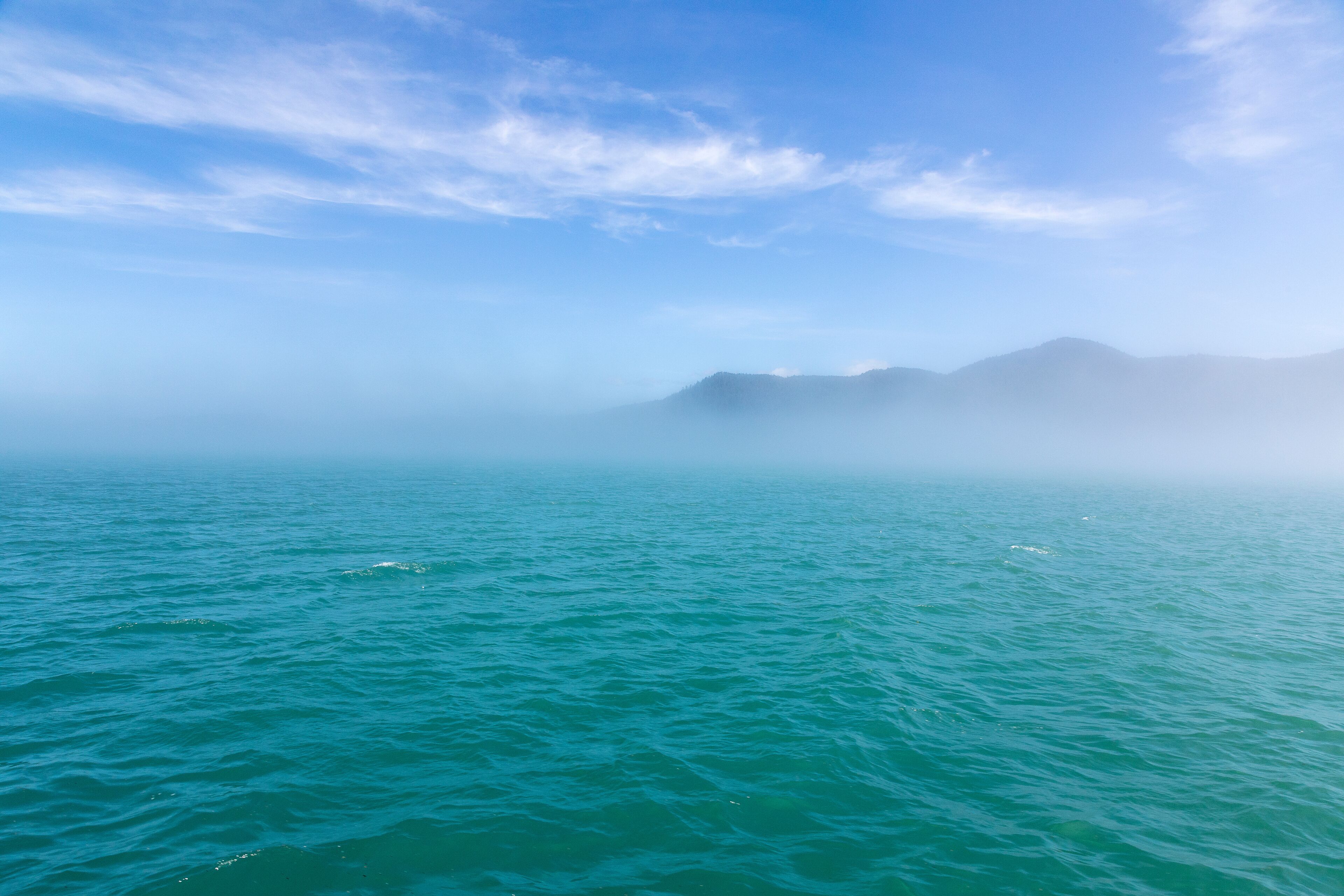 A calm sea with distant mountains and a clear sky.