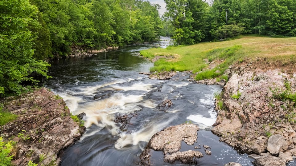 A fast-flowing river surrounded by dense green forest and rocky terrain.