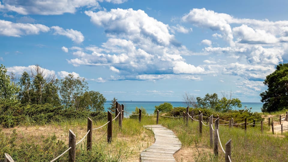A wooden boardwalk leading to a beach with a clear sky and clouds.