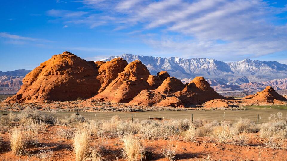 A desert landscape with red rock formations and a distant mountain range.