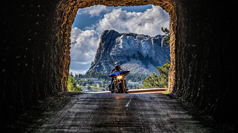 A motorcycle rider on a road tunnel with a mountain in the background.