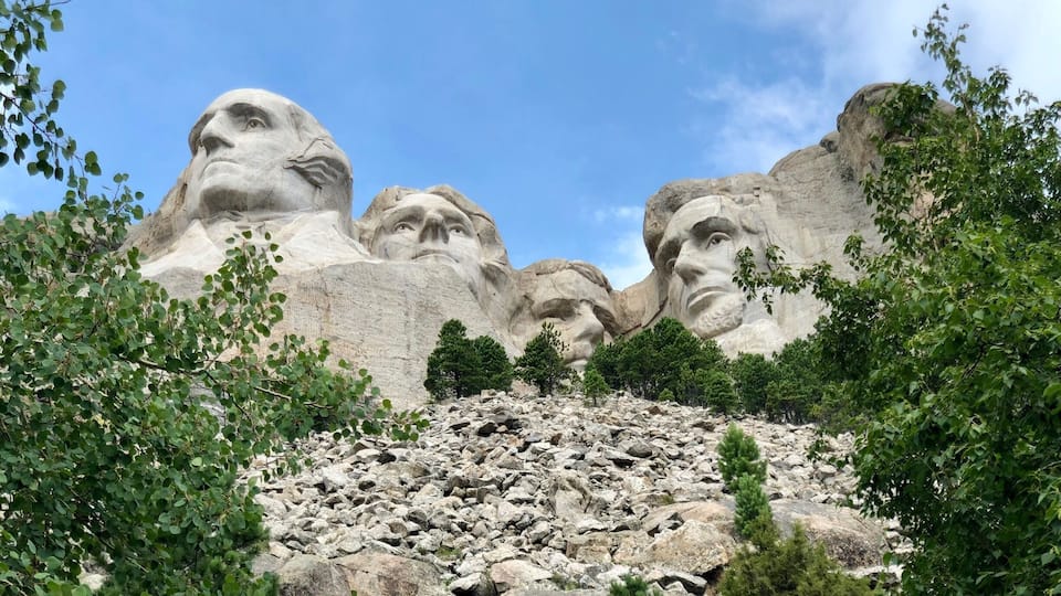 A large mountain with carved faces, surrounded by trees and rocky terrain.