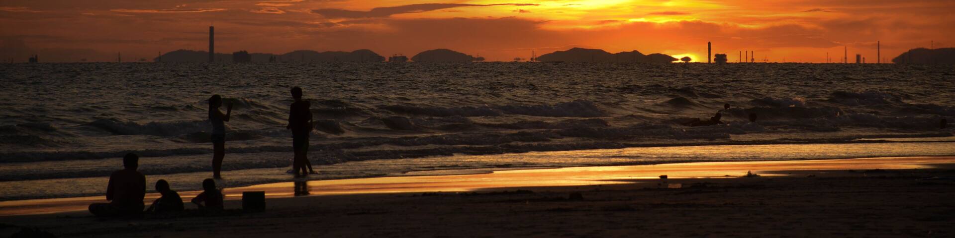 A sunset over a beach with people sitting and standing on the sand.