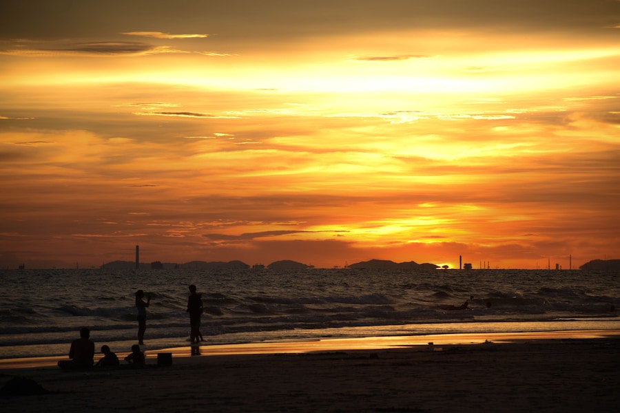 A sunset over a beach with people sitting and standing on the sand.