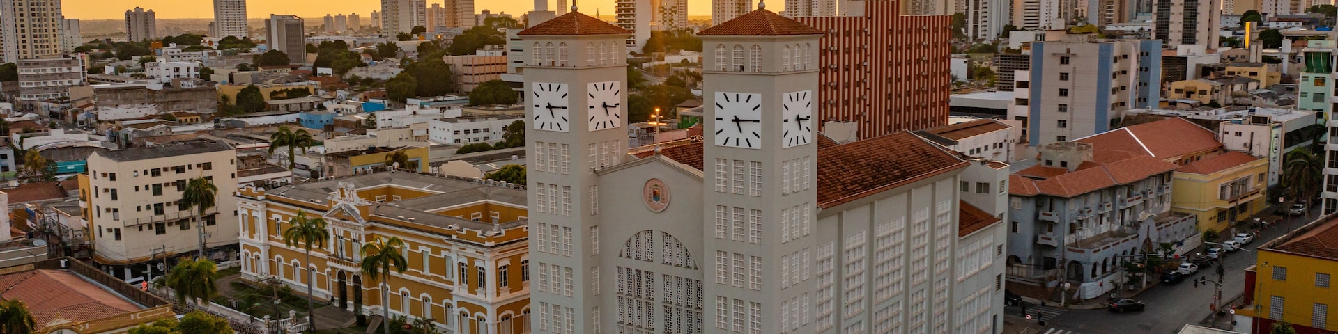 Paisagem urbana com uma torre do relógio imponente e um pôr do sol ao fundo.