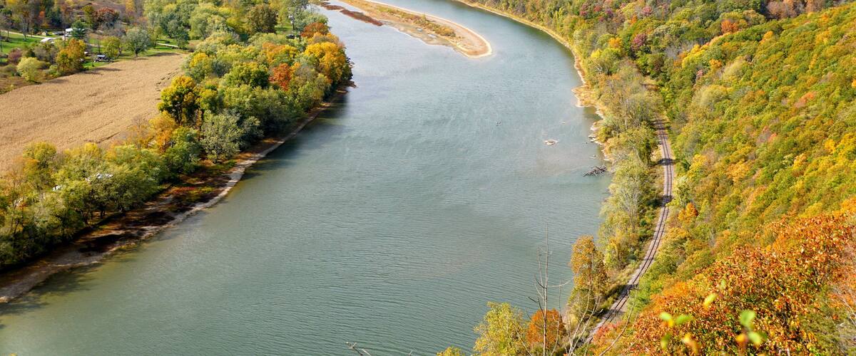 A river winding through a valley with autumn foliage, surrounded by hills and a railway track.